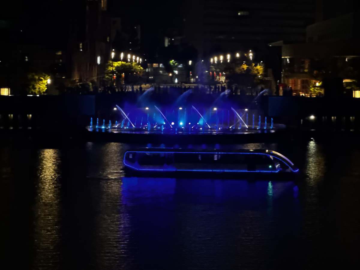 夜の運河を進む青いLEDの遊覧船と噴水